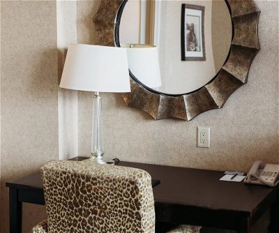 Modern hotel workspace featuring a leopard-print chair, round decorative mirror, and a lamp on a sleek desk.