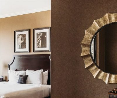Elegant hotel room featuring a wooden headboard, white bedding, decorative mirrors, and framed art on warm-toned walls.